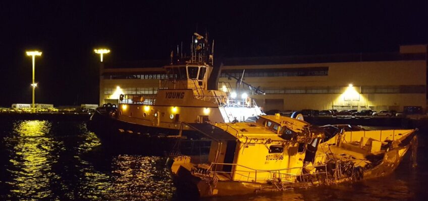 Partially submerged boat beside rescue vessel at night